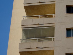 El cerramiento exterior transparente de una terraza situada en un piso alto junto a una playa española.